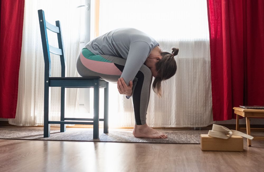 young woman in relaxing yoga pose called balasana or child pose sitting on chair in the living room.